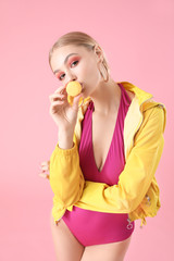 Beautiful fashionable woman with macaron on color background