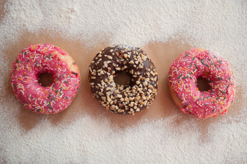 Three delicious doughnuts in pink and chocolate glaze are on a craft background, sprinkled with powdered sugar. Sweet food, fast food, obesity, pleasure