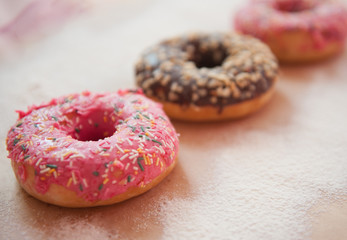 Three delicious doughnuts in pink and chocolate glaze are on a craft background, sprinkled with powdered sugar. Sweet food, fast food, obesity, pleasure