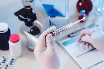 Fototapeta premium Nurse fills the form after coronavirus test. Analysis of test tube with a sample. Tube of biological sample contaminated by Coronavirus. Positive results. Medical exam. Epidemiology. Pandemic. 