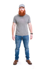 A strong young man with a large beard wearing baseball cap, t-shirt and jeans isolated on a white background