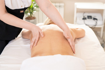 Unrecognizable therapist stroking back of woman while performing body massage at SPA procedure