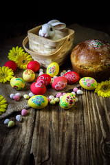 Traditional holiday composition. Hand painting Easter eggs with orthodox sweet bread on a dark wooden table. With rabbit figure. Selective focus.