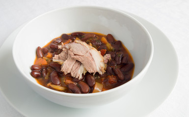a bowl of bean stew with vegetables decorated with ham