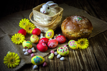 Traditional holiday composition. Hand painting Easter eggs with orthodox sweet bread on a dark wooden table. With rabbit figure. Selective focus. Close-up.