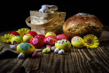 Traditional holiday composition. Hand painting Easter eggs with orthodox sweet bread on a dark wooden table. With rabbit figure. Selective focus.