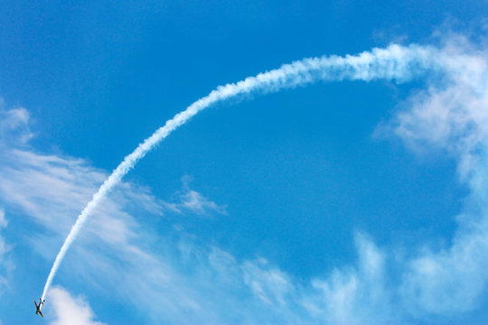 Avi&atilde;o monomotor fazendo acrobacia a&eacute;rea soltando fuma&ccedil;a em c&eacute;u azul