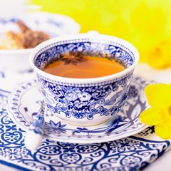 A cup of tea with anise star. White and blue dishes and yellow daffodils