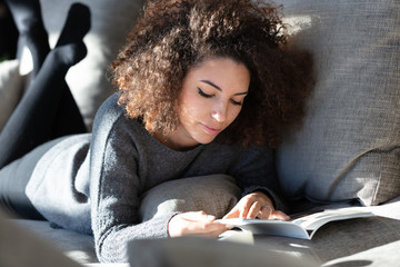 Young woman lying on lounge reading magazine