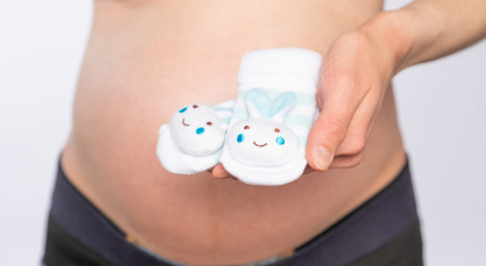 Pregnant woman holds small socks on the background of the abdomen