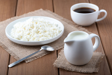  Cottage cheese in a plate, coffee and milk on a wooden table