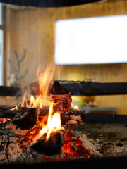 The grill is indoors, the firewood, naked fire, red coals, preparation of coals for grill, window is on background