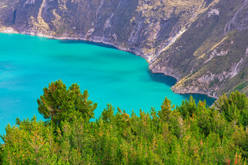 Turquoise waters of the Quilotoa crater lake with pine trees in the foreground, South of Quito, Ecuador.