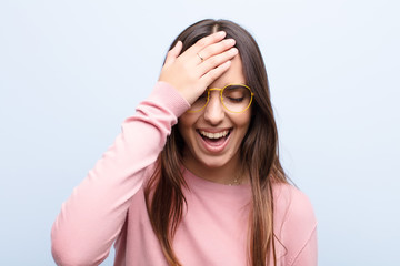 young pretty woman laughing and slapping forehead like saying d‚Äôoh! I forgot or that was a...
