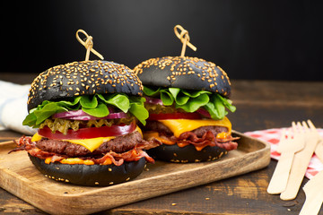 Two huge black hamburgers on dark wooden background