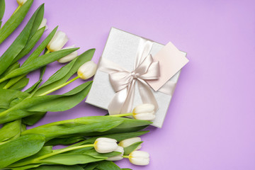 Gift and beautiful flowers on color background