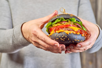 Female hands hold a black hamburger