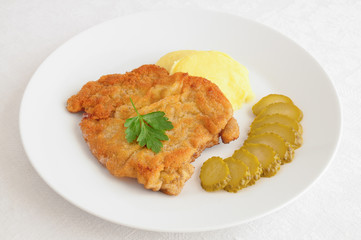 breaded schnitzel with mushed potato and pickled cucumber