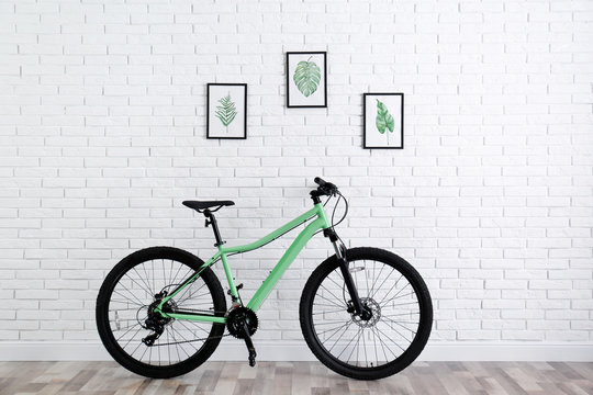 Modern green bicycle near white brick wall indoors