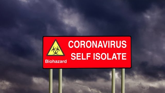 A red road sign warning of the biohazard Coronavirus Covid-19 virus infection and illness with stay at home advice under a time lapse of gathering dark storm clouds. Lockdown and self isolation.