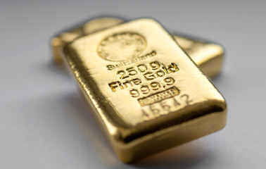 Two gold bullions weighing 250 grams each on a grey background. Selective focus.