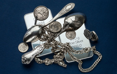 Silver bullion, silverware, jewelry and old coins on a dark blue background.