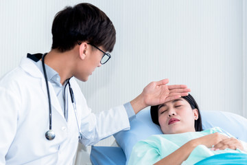 The Asian male doctor used the back of his hand to touch the forehead of a female patient, lying in...