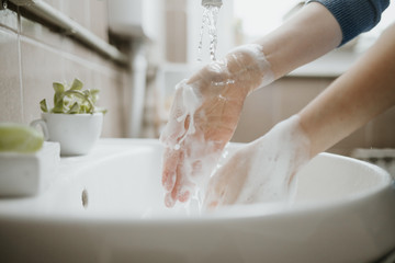 Closeup of a woman washing her hands in bathroom to prevent Covid-19 viral infection. Recommended washing with soap and running water during coronavirus pandemic.