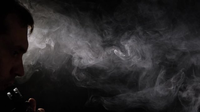 A man smokes a vape on a black background close-up. Slow motion