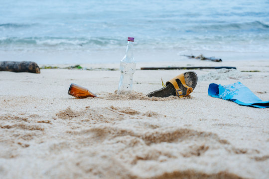 Bottles And Shoe Buried In White Sand Beach Of An Ocean Shore