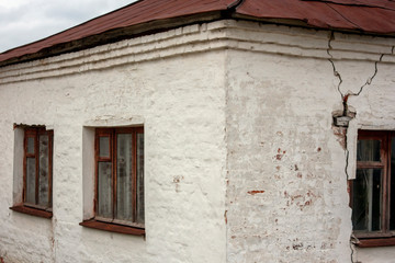 Corner of the wall of an old house. Crack on the whitewashed wall of the house. The house is white with a brown roof. Three windows in the house under the roof..