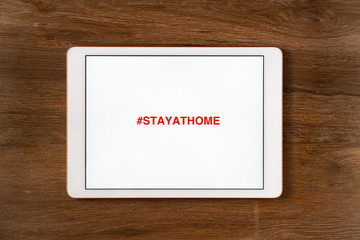 Stay Home inscription on tablet, mobile phone. Stay at home advice to stop coronavirus COVID-19 spreading. On wooden background. Concept how to stop the coronavirus from spreading