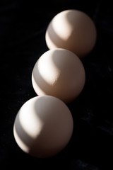 Easter decoration. Closeup of three eggs in linght and shadow on the black background.