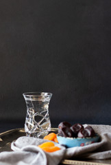 Iftar, evening meal during month of Ramadan. Glass of water, dates, dried apricots on metal tray with grey napkin, dark background. Vertical orientation, copy space.