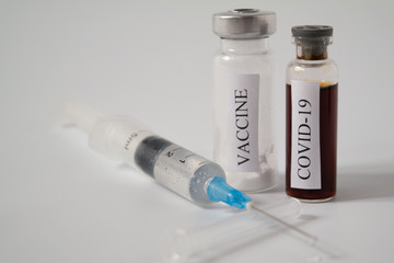 A medical syringe and test tube with a liquid labeled COVID-19 and a white powder labeled vaccine. Flask with a virus test and an antiviral drug. Concept of vaccination and medicine for a disease.
