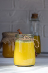 Glass jar with a healthy drink of golden milk made from turmeric, milk and pepper on a white wooden background. Prevention of diseases and viruses.