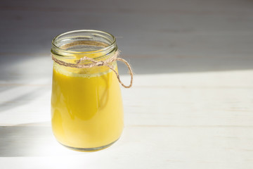 Glass jar with a healthy drink of golden milk made from turmeric, milk and pepper on a white wooden background. Prevention of diseases and viruses.