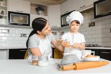 Happy mother and her little son shaking raw eggs in bowl before making dough for homemade pastry in the kitchen