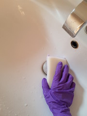 Closeup of lady wearing glove using sponge to wash sink.  Hygiene concept.