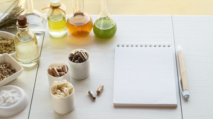 Various capsules with dietary supplements, ingredients for their creation and a notebook with a pen