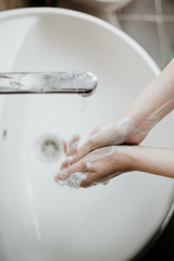 Closeup of a woman washing her hands in bathroom to prevent Covid-19 viral infection. Recommended washing with soap and running water during coronavirus pandemic. Top shot view.