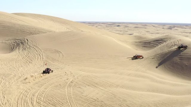 Aerial follow view, all terrain vehicles ATVs in desert driving over sand dunes