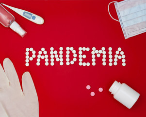 Text phrase Pandemia on a red background with medicines, hand antiseptic, thermometer and protective mask.