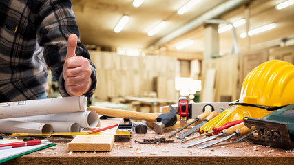 Close-up. Carpenter in the carpentry workshop makes OK sign with thumb up. Construction industry.