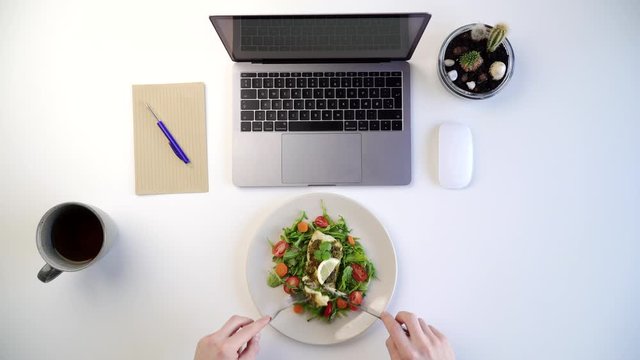 Top view of male eating healthy salad at work place next to laptop 