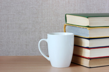 stack of color covered books and a white mug on the table.