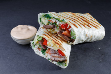 Shawarma with vegetables and meat on a wooden stand.