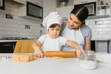 Little boy helping his mother with the baking in the kitchen standing at the counter alongside her kneading the dough for the pie