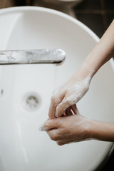 Closeup of a woman washing her hands in bathroom to prevent Covid-19 viral infection. Recommended washing with soap and running water during coronavirus pandemic. Top shot view.