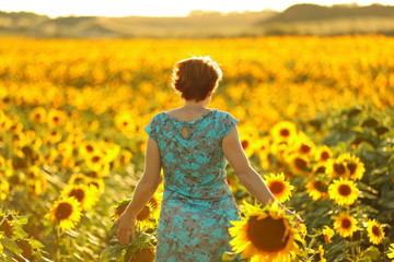 Fototapeta premium woman in blue dress happily walking through a yellow field ofsunflowers